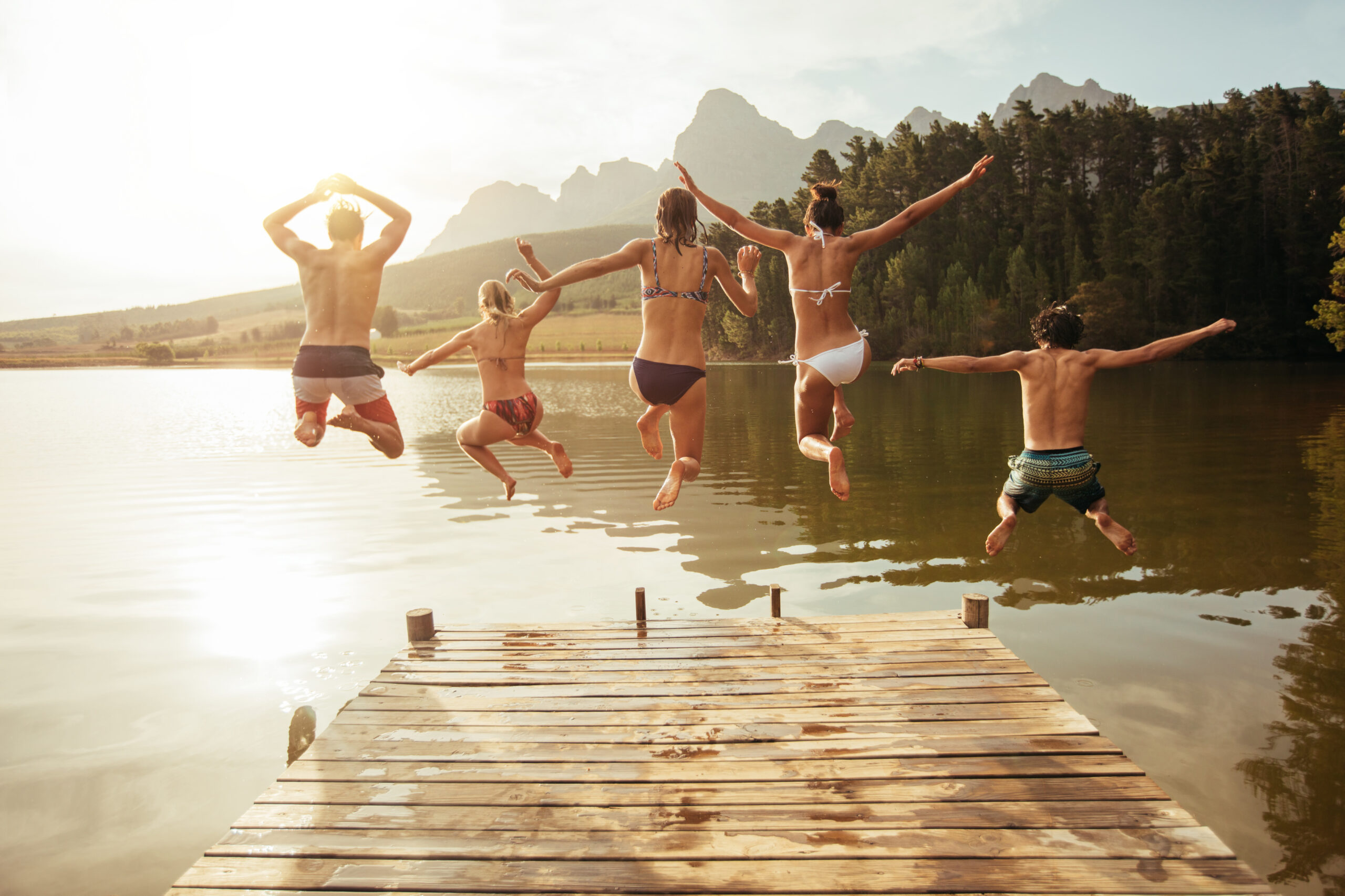 young friends jumping into lake from a jetty