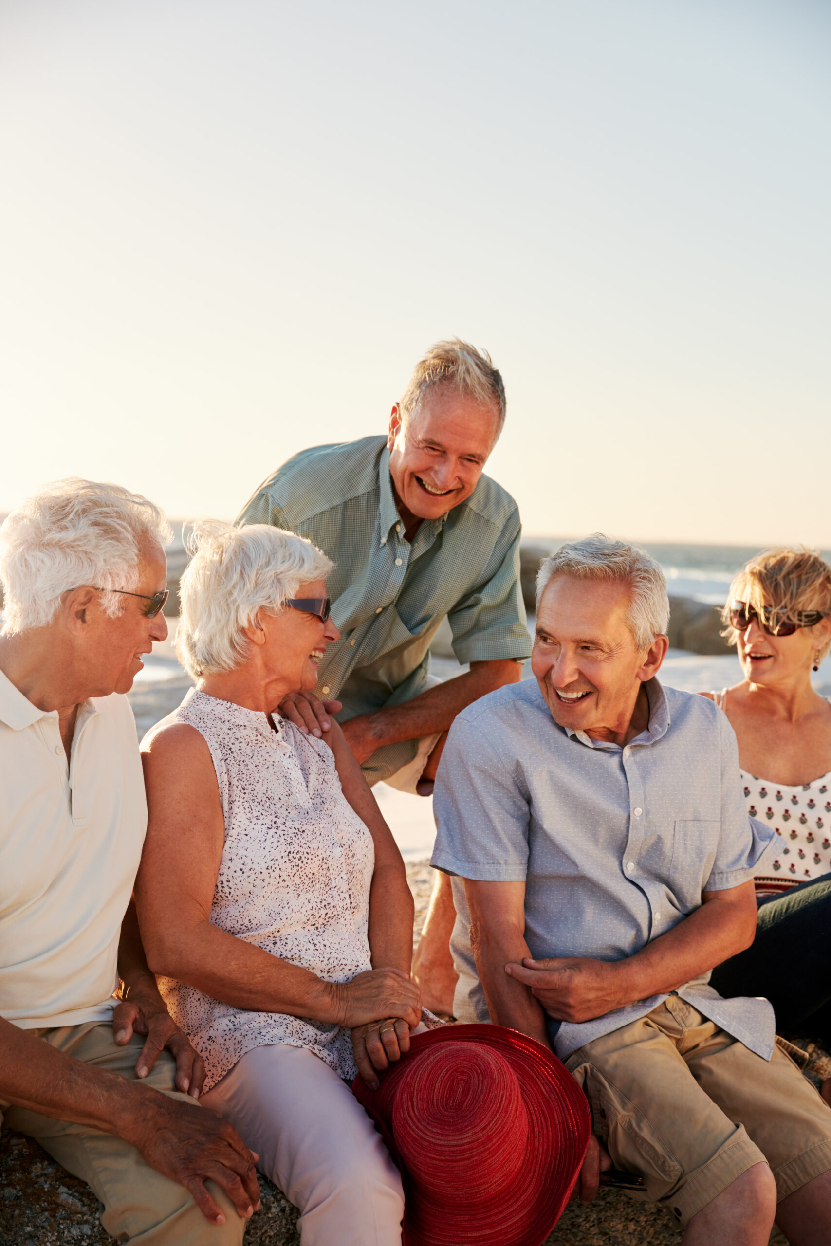 Group Of Senior Friends Sitting On Rocks By Sea On Summer Group Vacation